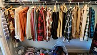 Wide view of ladies clothing hanging on racks showing sweaters, shirts, flannel shirts, pants, and crochet blankets folded and stacked on shelves.