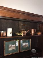 Shelf display of copper and brass items including coffee pot, brass tiger figurine, white mug with bee, copper containers.