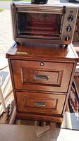 Front view of wood filing cabinet showing two drawers with metal handles. Key in lock on top drawer. Small toaster oven placed on top of the cabinet.