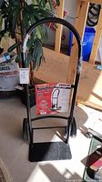 Full view of the black steel hand truck standing upright showing curved handle and platform.