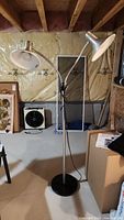 Full view of the two light floor lamp, showing the lamp's shape, black round base, and overall height, set in basement space.