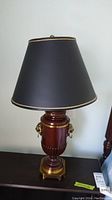 Side view of the wood and brass table lamp with black shade and gold trim, showing the decorative brass accents and wooden base.