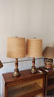 Two table lamps with burlap style shades positioned side by side on wooden cabinet.