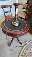 Front view of the wood round table showing leather insert top, single drawer, and leg design with a lamp on top.