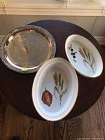 Photo of two Royal Worcester ceramic dishes with botanical designs and a round metal tray on a wooden table.
