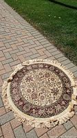 Round machine made rug outdoors on pavers showing full design and fringe edges