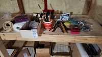 Photo of wooden shelf holding various items including soldering iron, brushes in a cup, boxes with screws/nails, rope and paper towel roll