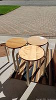Photo of three wooden round seat stools with white metal legs placed on a rug in sunlight.