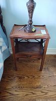 Front view of the antique wooden side table showing carved details, drawer, and top surface with wear.