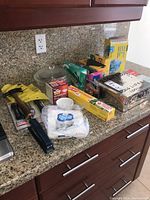Wide view of countertop showing tools and household items including hammer, stapler, various boxed supplies, gloves, and plastic wrap.