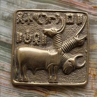 Close-up photo of the bronze paperweight showing the detailed bull figure and surrounding symbolic carvings on a textured surface.
