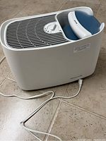 White and blue Honeywell humidifier with power cord on tiled floor.