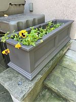 Side view of gray rectangular planter with yellow pansy flowers and green plants, showing the overall design and structure.