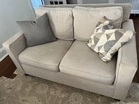 Front view showing two seat cushions, two back cushions, and three throw pillows on oatmeal fabric upholstery.