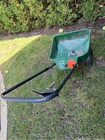 Side and top view of green Scotts Turf Builder Seeder on grass with black handle and orange spread adjustment dials.