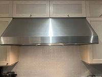 Front view of stainless steel range hood installed under cabinetry.