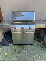Three-burner stainless steel BBQ grill front view showing hood, control panel, side table, cabinet base and wheels