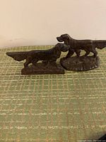 Pair of cast iron Irish Setter dog bookends shown side by side on green patterned fabric.<br>One dog on a rectangular base, the other on an oval base, both with detailed fur texture and poses.