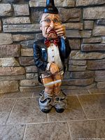 Full view of butler tissue holder figurine standing on floor against stone wall. Showing front with facial expression and clothing details.