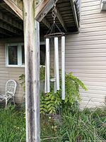 Full view of the weathered hand crafted butterfly wind chimes hanging outdoors beneath wooden structure