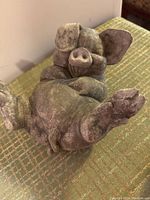 Concrete laughing pig statue lying on back showing face and feet with textured concrete surface.