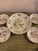Front view of large central bowl surrounded by four smaller plates, all with floral and bird motifs accented in gold.