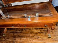 Top view of coffee table showing beveled glass inset, wooden frame, and brass claw feet on carved legs.