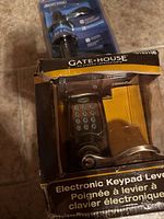 Electronic keypad lever lock in a damaged Gate House box showing numeric keypad and lever handle.