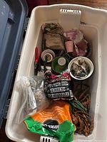 White plastic bin containing various gardening supplies including multiple bags of soil, pruning shears, small pots, and twine material.