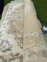 Rolled view of beige area rug showing floral pattern and woven underside.