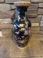 Front view of large porcelain vase with black background and colorful floral and bird designs, gold accents around rim.
