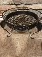 Metal plant stand front angled view showing lattice bottom and curled metal legs with decorative scroll work