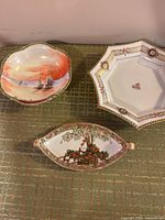 Three Nippon porcelain pieces displayed on a green patterned fabric: round scalloped bowl, octagonal dish, leaf-shaped dish.