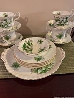 Photo showing stacked teacups on saucers, snack plates, shell-shaped bowl, and scalloped treat platter with floral and gold trimming.