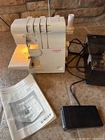 Overall view of Singer Ultralock Serger, foot pedal, and operator’s guide on tile floor