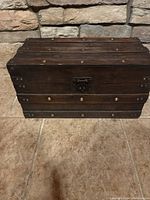 Front view of small vintage wooden trunk showing metal rivet accents and central latch.