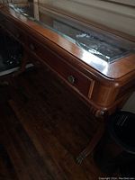 Side view of wooden sofa table showing beveled glass top and curved legs with decorative feet.