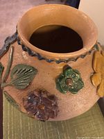Photo showing top view of terra-cotta pot with raised flower and leaf decorations, showing color and detail.