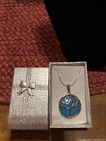 Tree of Life pendant on turquoise colored stone in silver necklace chain inside a silver textured box with a bow on top.