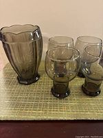 Photo showing four smoky grey glass cups and one vase with scalloped rim and vertical ridges.