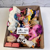 Box filled with assorted vintage to newer collectible toys including dolls, plastic horses, cartoon character figures, and toy accessories.