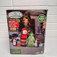 Front of box showing illustration of assembled inflatable Santa and Friends scene outdoors at night with lights on.