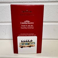 Front view of the red Hallmark Keepsake box with text describing the ornament as the RV from National Lampoon's Christmas Vacation titled "That's An RV", including a small photo of the ornament.