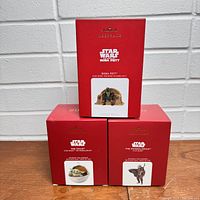 Three red Hallmark Keepsake boxes shown with Star Wars themed ornaments inside. One box on top with Boba Fett image, two boxes below with images of The Child and the Mandalorian wolf companion.