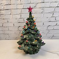 Front view of ceramic Christmas tree showing colorful plastic light bulbs and pink star on top, plugged in but not illuminated.