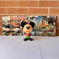 Photo showing two Disney pictorial books and a vintage Mickey Mouse talking pull-string toy in front of a brick wall.
