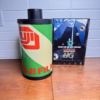Front view of the vintage Fuji Film store display showing the large green and beige Fuji Film roll replica and the black promotional panel with film strip design and colorful Fujicolor Super HG advertisement.