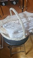 White and beige crochet pieces folded inside a white wicker basket shown on a stool