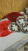 Photo showing red plastic fruit and vegetable dip tray with 4 compartments, 4 smaller red sparkle trays, and several holiday print plates with Christmas designs