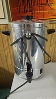 Front view of stainless steel coffee urn with black handles and spigot on table